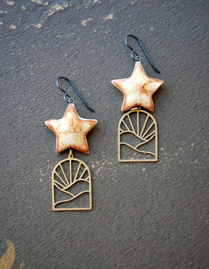 a pair of star shaped earrings on a stone surface
